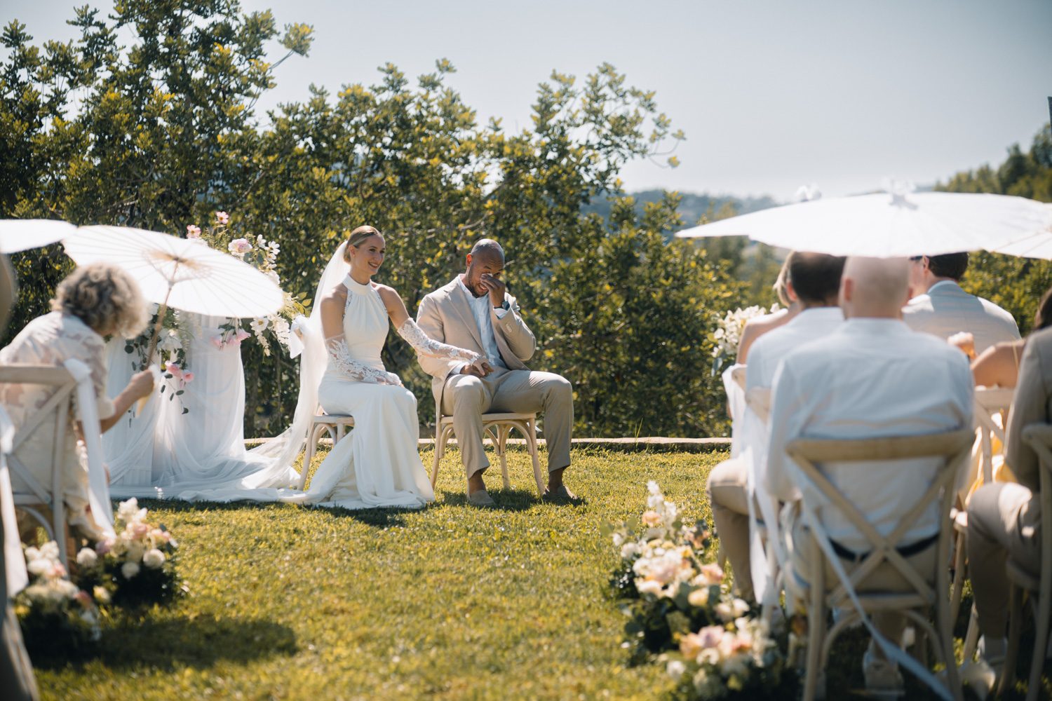 Bride and groom seated together during an outdoor wedding ceremony.