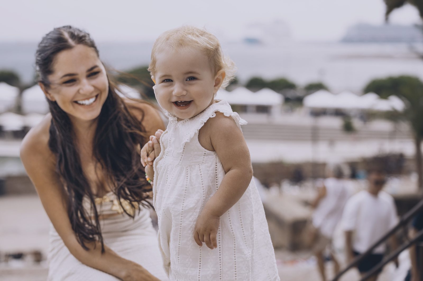 Mother and young child smiling together by the sea.