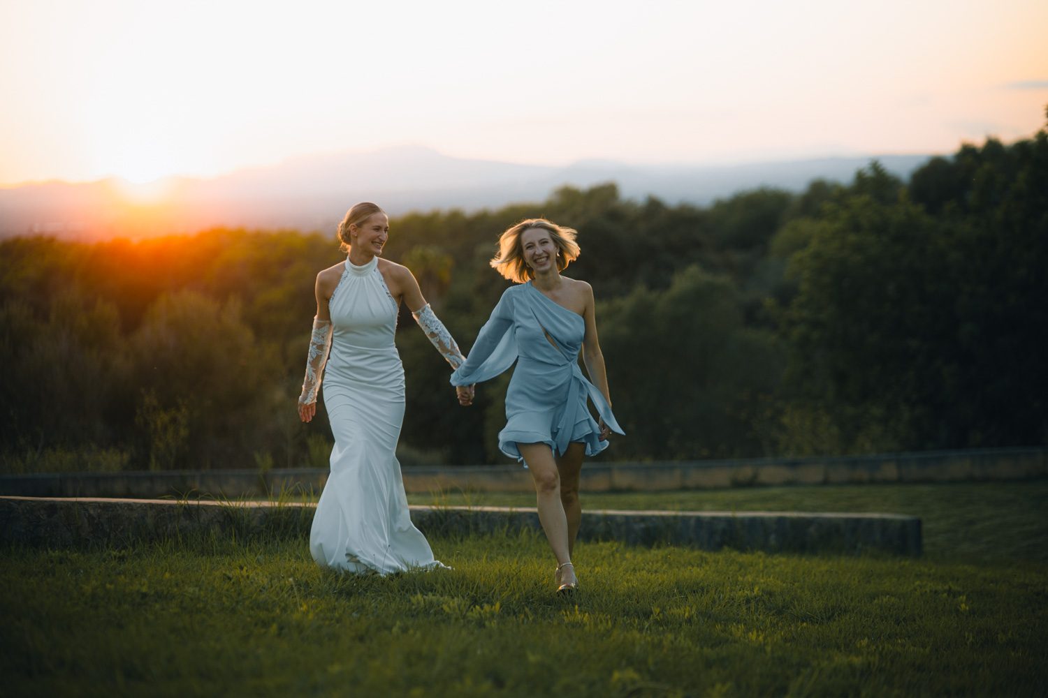 Bride running and laughing with a friend in evening light.