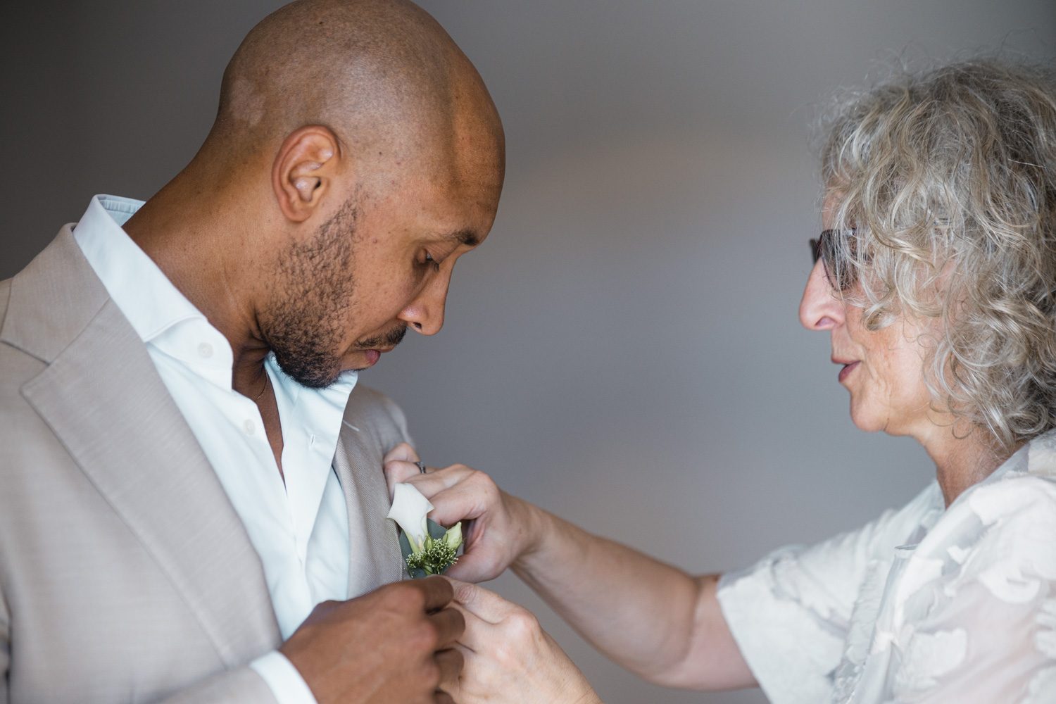 A family member fastening the groom’s boutonniere during preparations.