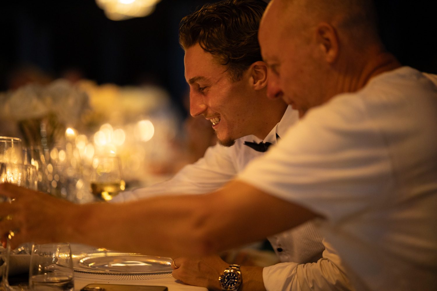 Newlyweds leaning together at the candlelit dinner table.