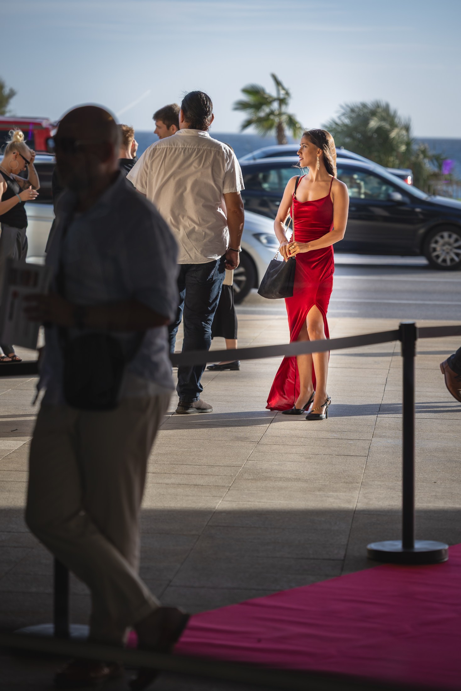 Woman in a red dress arriving at an event with other guests nearby.