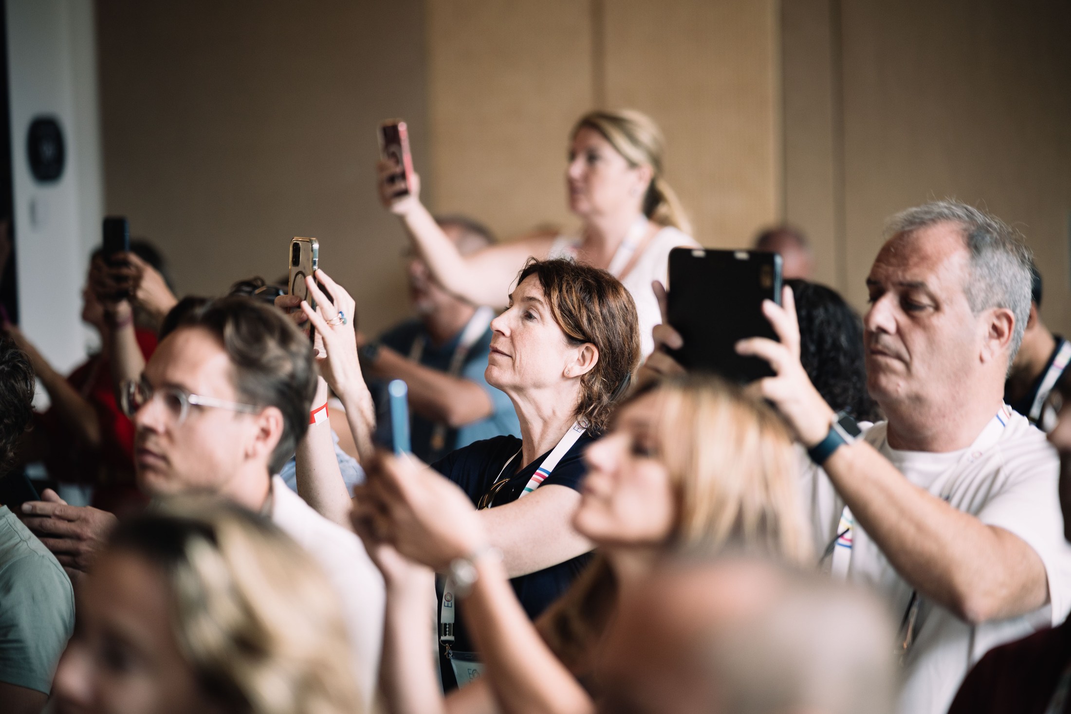 Audience members photographing a speaker with their phones.