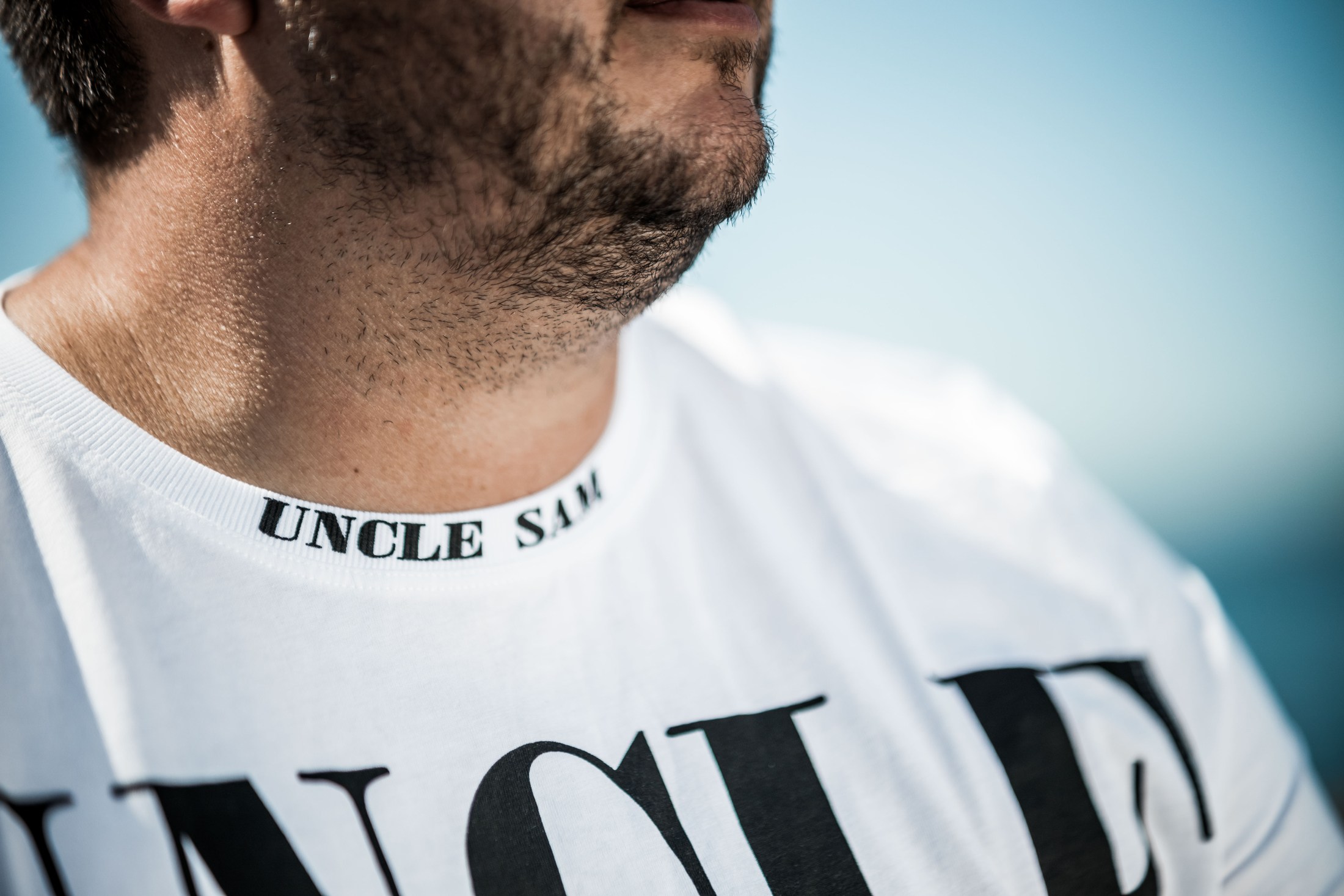 Man in sunglasses wearing a white T-shirt outdoors.