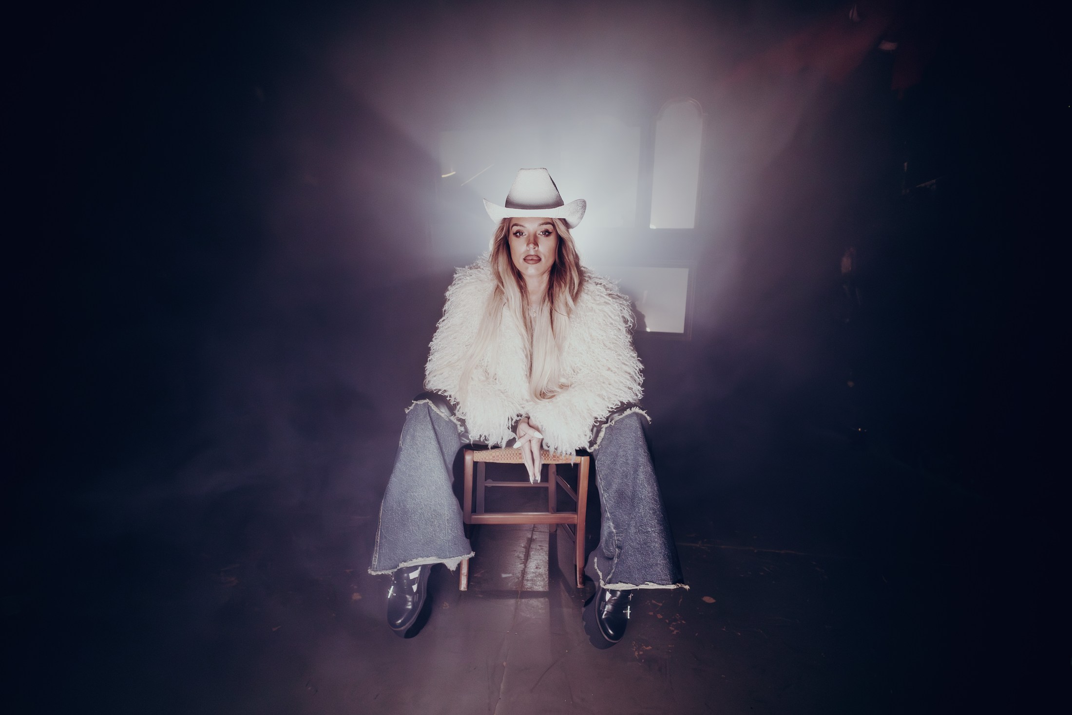 Woman in a white hat seated under a spotlight during a performance.